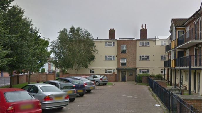 View of a residential building with a parking lot and several cars in front.