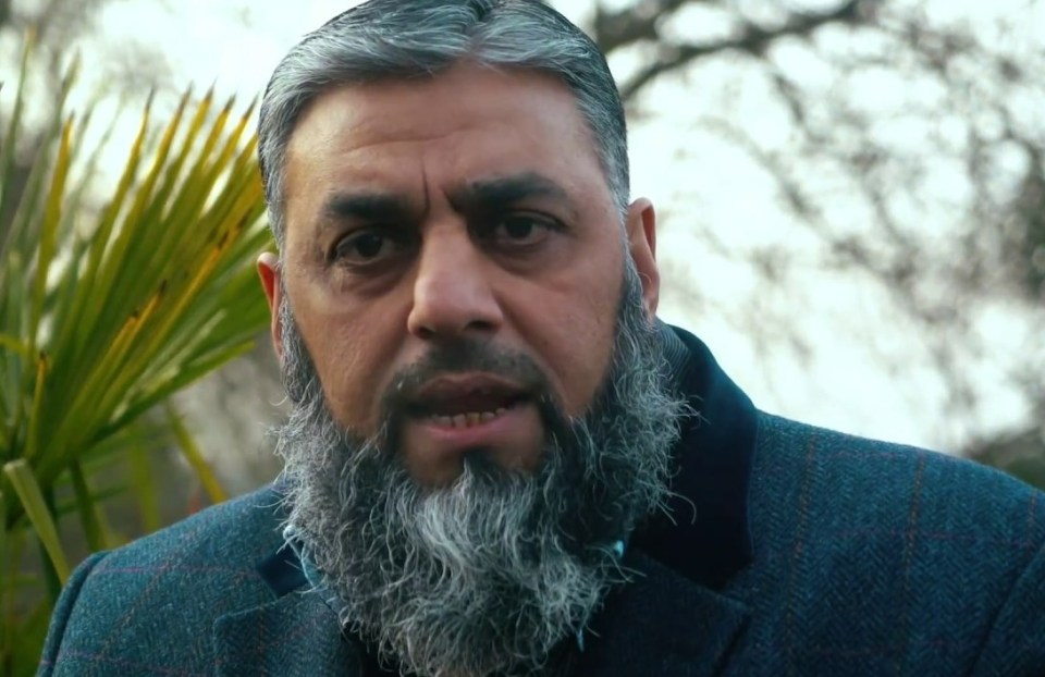 A man with a gray beard and hair, wearing a light blue shirt.