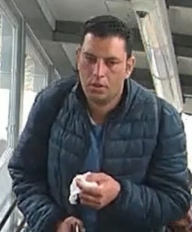 A man with dark hair in a dark blue puffer jacket holding a white tissue in his right hand.