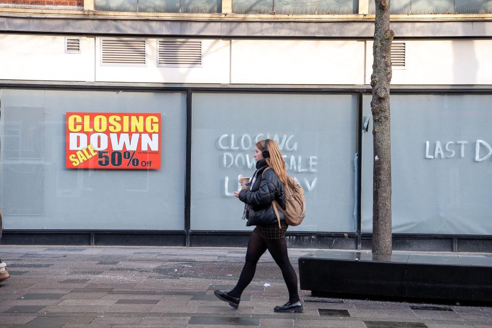 A "Closing Down Sale 50% Off" sign in a store window with a pedestrian walking past in Slough, UK.