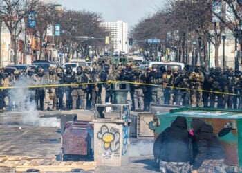 Protesters take cover behind overturned trash containers as a line of federal agents forms a barricade across a downtown street during clashes following the fatal shooting of a demonstrator earlier in the day, on Jan. 24, 2026, in Minneapolis, Minnesota.