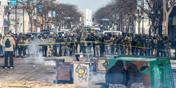 Protesters take cover behind overturned trash containers as a line of federal agents forms a barricade across a downtown street during clashes following the fatal shooting of a demonstrator earlier in the day, on Jan. 24, 2026, in Minneapolis, Minnesota.