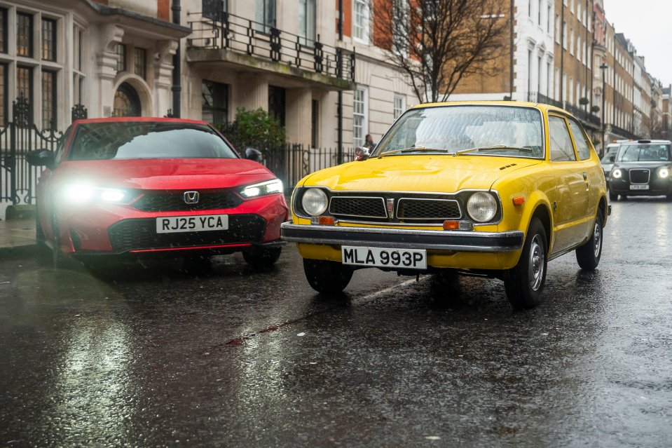 A modern red car with bright headlights facing an older yellow car on a wet city street.