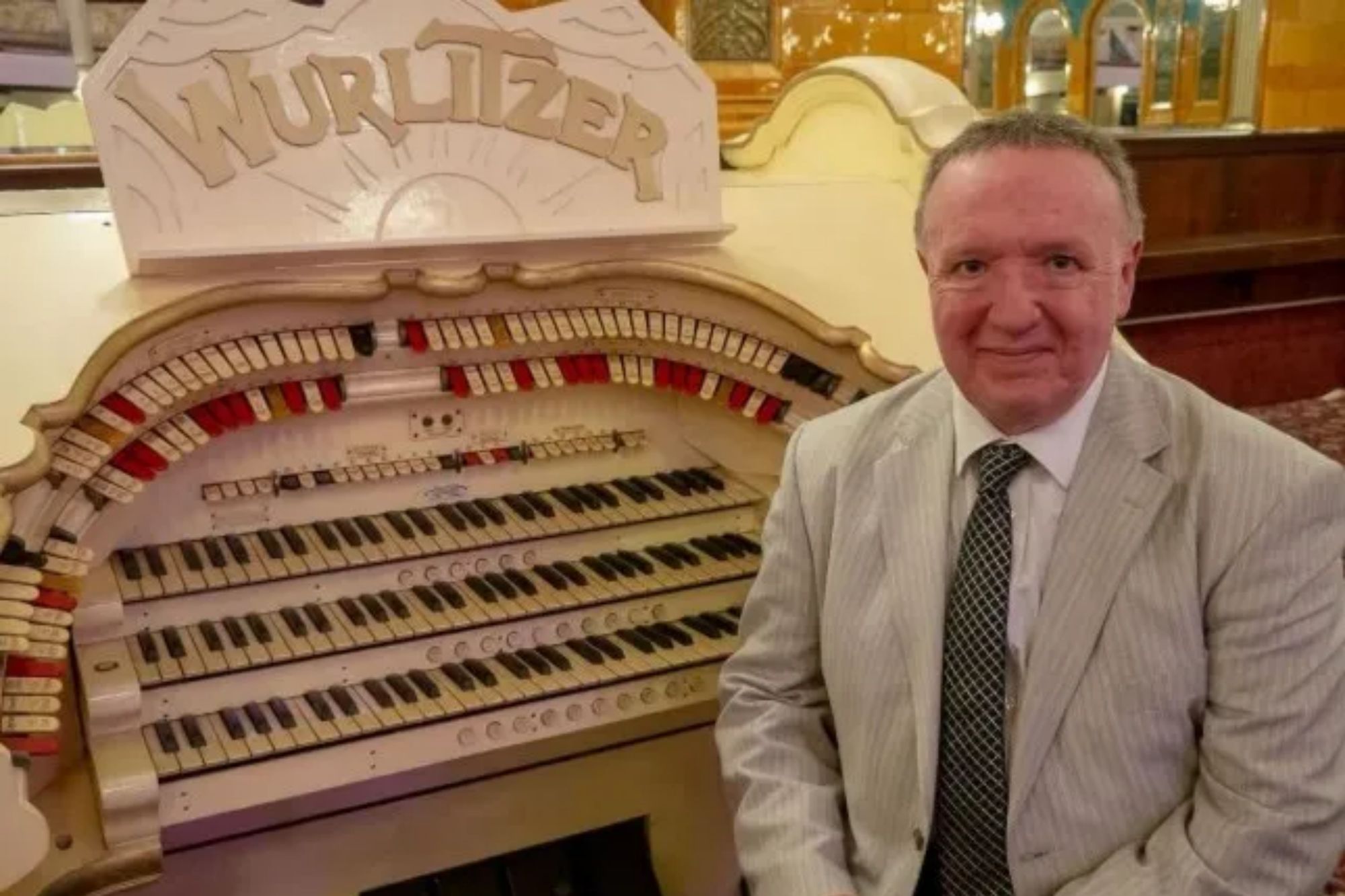 An image collage containing 1 images, Image 1 shows A man in a suit sitting next to a white Wurlitzer organ