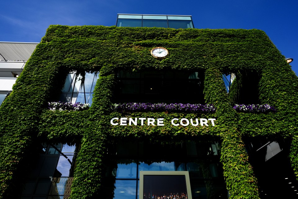 Exterior of the Wimbledon Centre Court building covered in green ivy, with a clock near the top and the words "CENTRE COURT" in white letters across the middle.