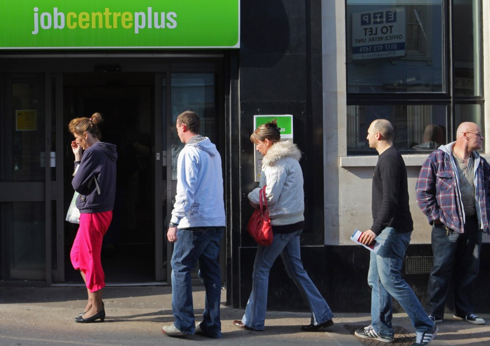 Pedestrians walk past a Jobcentre Plus building, with the green sign visible above the entrance.