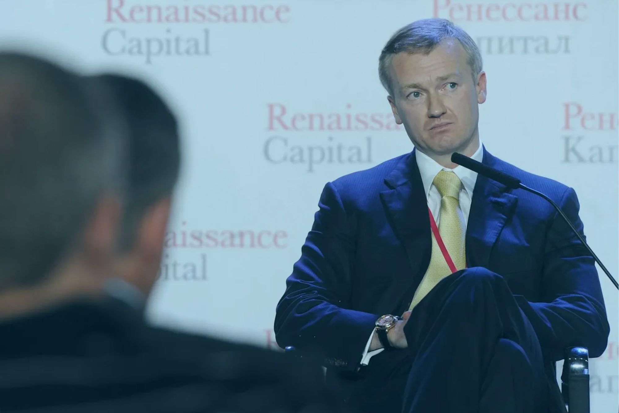 An image collage containing 1 images, Image 1 shows Vladislav Baumgertner, a Russian businessman, sits in a dark suit and yellow tie, speaking into a microphone