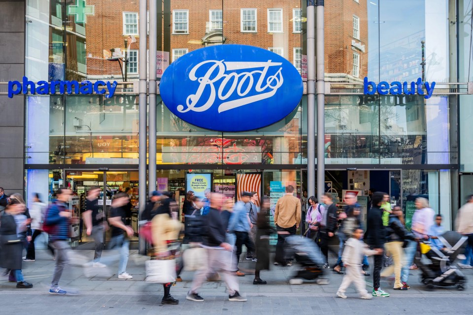 A busy Boots pharmacy with people walking past the entrance, blurred due to motion.