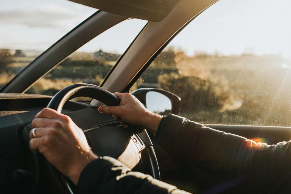 Hands on a steering wheel in a car with sunflare.