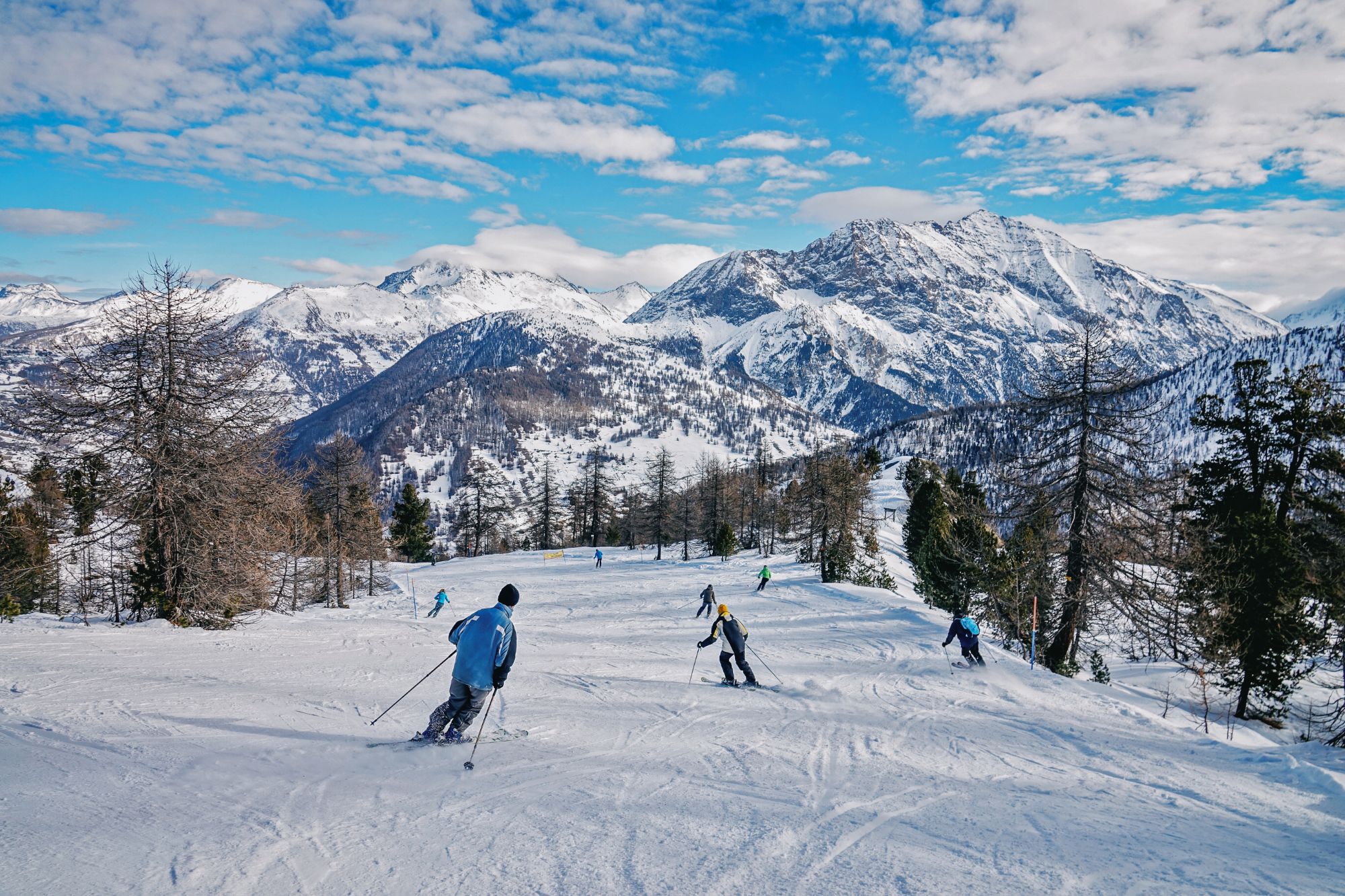An image collage containing 1 images, Image 1 shows People skiing on a snowy slope at Claviere ski resort with mountains in the background