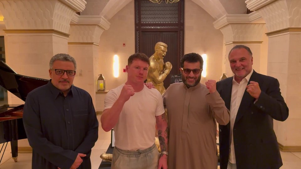 Canelo Alvarez and Turki Alalshikh with two other men, all raising their fists, in front of a golden boxer statue.