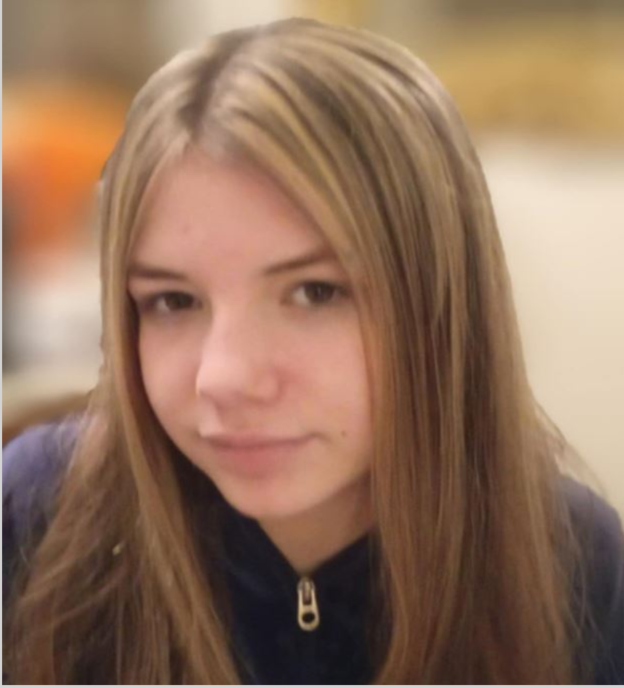 A young girl with long brown hair and highlights, wearing a navy blue zip-up jacket.