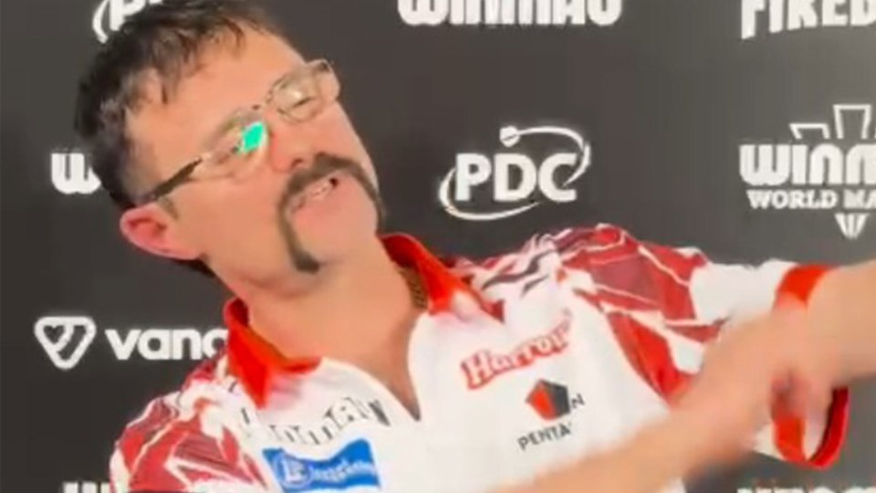 Darts player Peter Wright in a red and white shirt, glasses, and a mustache.