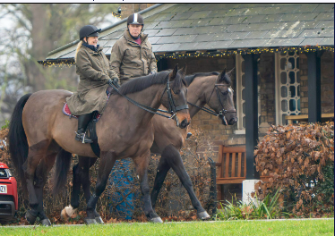 Two people riding horses past a house decorated with lights.