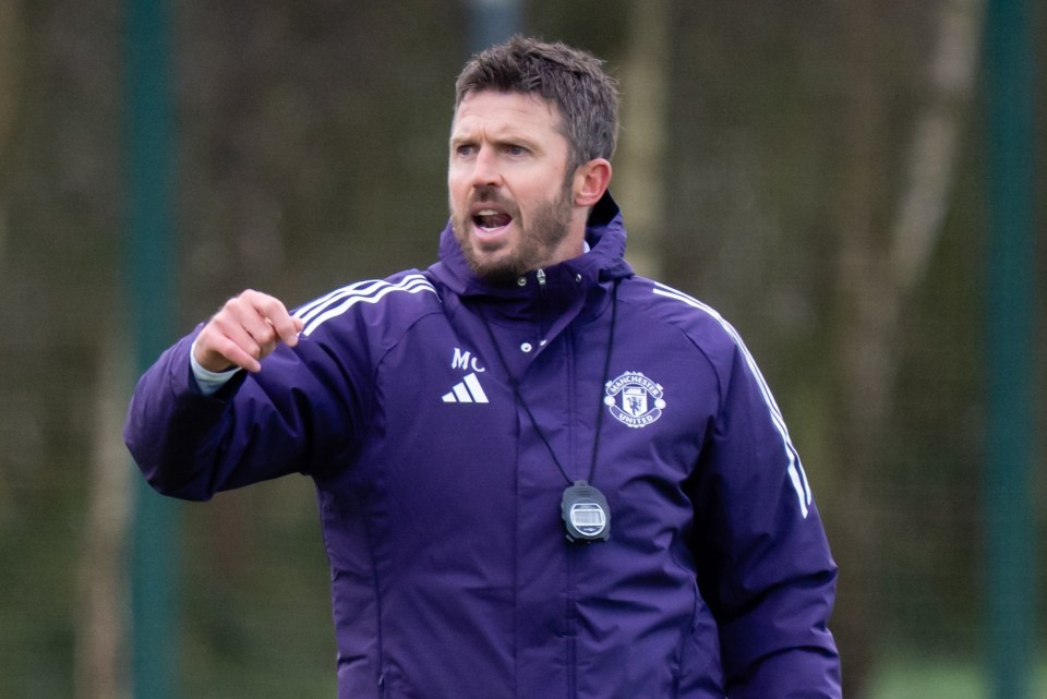 Manchester United Head Coach Michael Carrick in a purple jacket directing players on a soccer field.