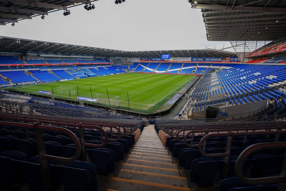 An empty Cardiff City Stadium with blue seats and a green football pitch.