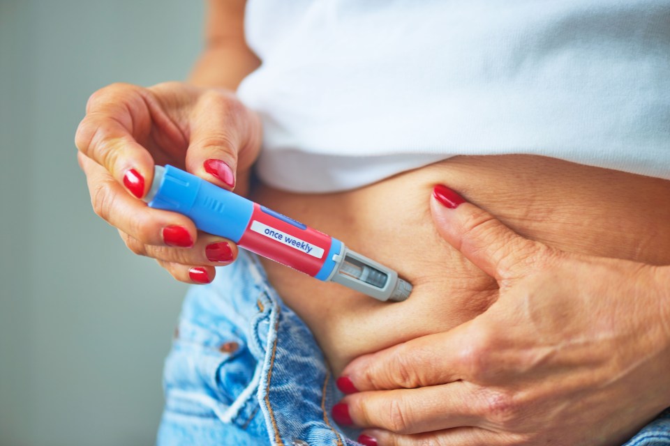 A woman injecting her abdomen with an Ozempic pen labeled "once weekly."