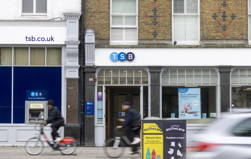 A TSB Bank branch in London, UK, with passersby and a street recycling bin in the foreground.
