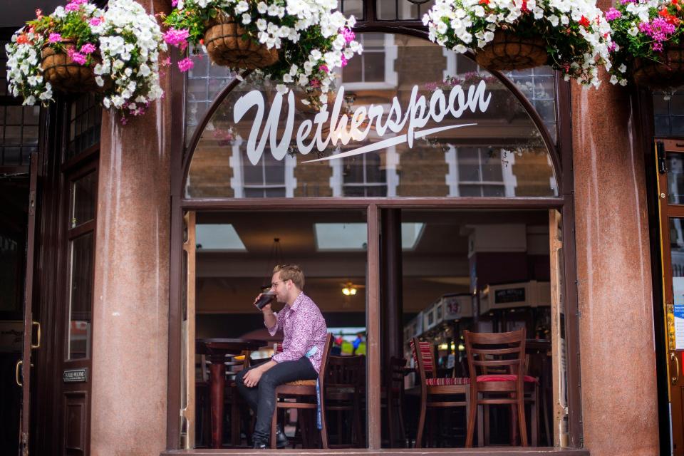 A man sitting inside a Wetherspoon pub in London, drinking from a glass.