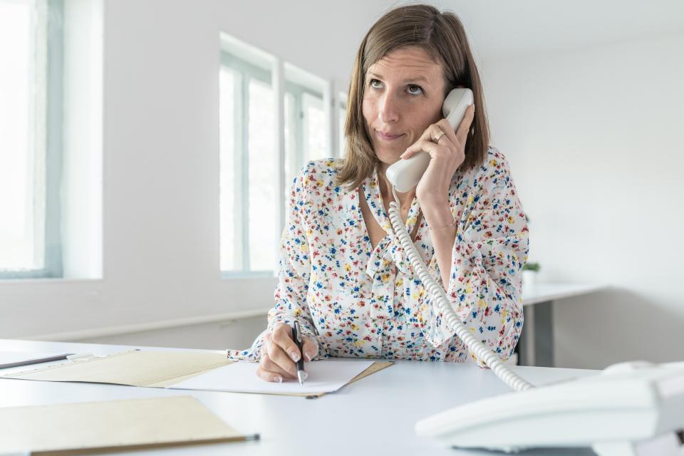 Young businesswoman sitting at her office desk with paperwork in front of her talking on a landline phone.