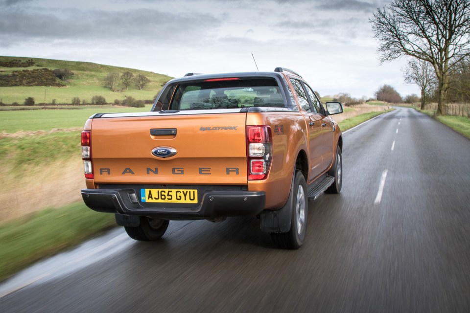 Rear view of an orange Ford Ranger Wildtrak pickup truck driving on a country road.