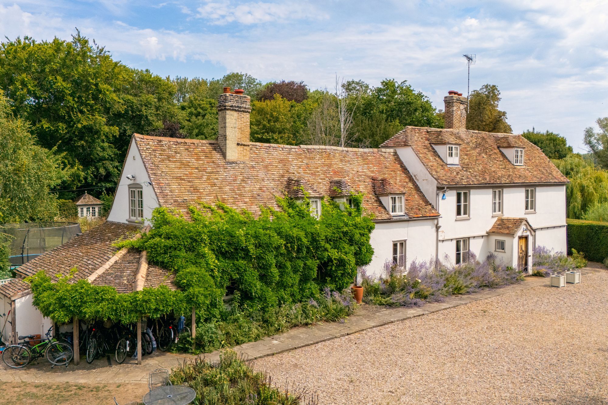An image collage containing 1 images, Image 1 shows Aerial view of the Grade II listed 7-bed property in Grantchester, a former mill house, with a gravel driveway and surrounding trees