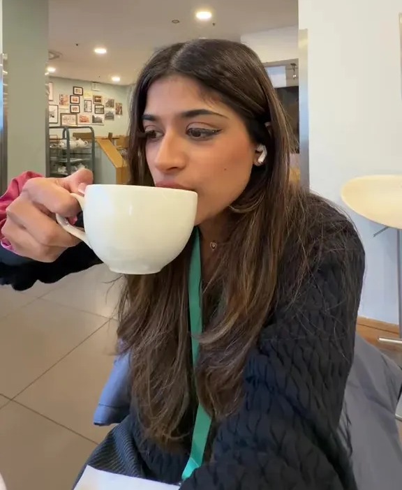 A young woman sips from a white mug, with text overlay "John Lewis FREE CAKE AND HOT DRINK!!"