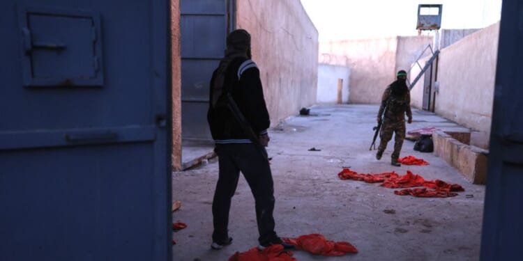 Syrian government fighters walk inside Al-Shaddadi prison, where red detainee suits lie on the ground, in the town of Shaddadeh, northeastern Syria, on Tuesday, a day after Syria's Interior Ministry said Islamic State group members escaped from the facility during clashes with the Kurdish-led Syrian Democratic Forces.