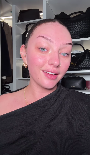 A woman with fair skin and blue eyes, wearing a black top, looks at the camera with a slight smile.