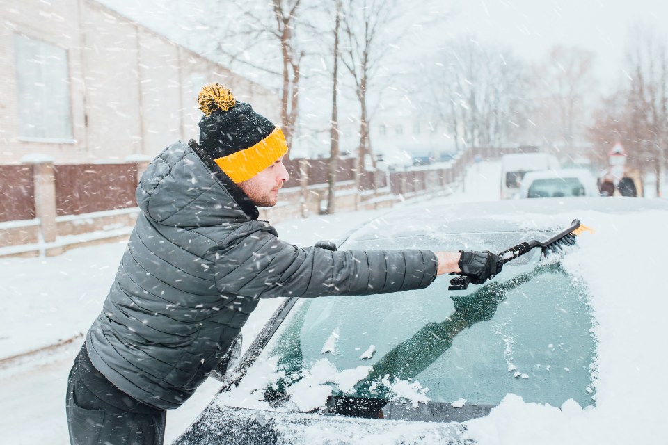 A man brushing a car brush from snow in the winter in the morning