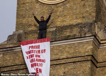 The protester raised his arms after securing the banner in place, which criticised the UK Government's response to the Iranian regime's murder of thousands of protesters