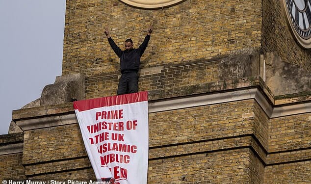 The protester raised his arms after securing the banner in place, which criticised the UK Government's response to the Iranian regime's murder of thousands of protesters
