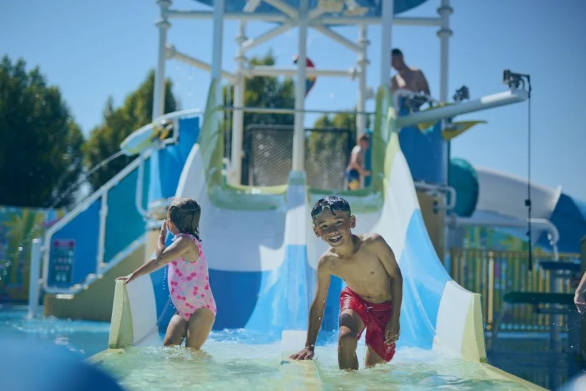 An image collage containing 1 images, Image 1 shows A boy and a girl playing in a water park, with blue and white water slides in the background