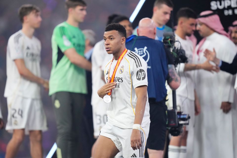 Kylian Mbappe wearing a white Real Madrid jersey and a silver medal around his neck.