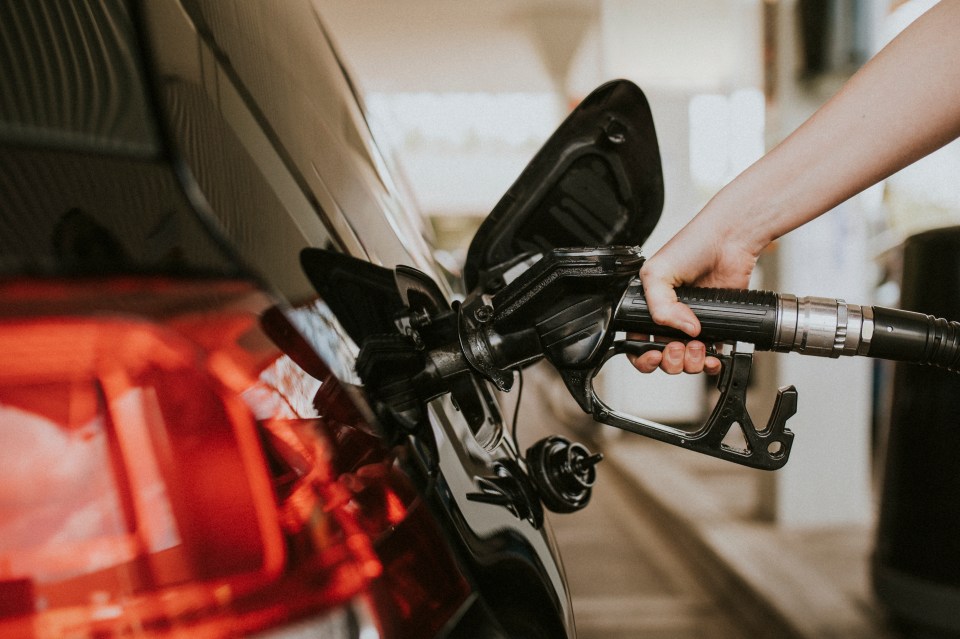 Person refueling a black car at a gas station.