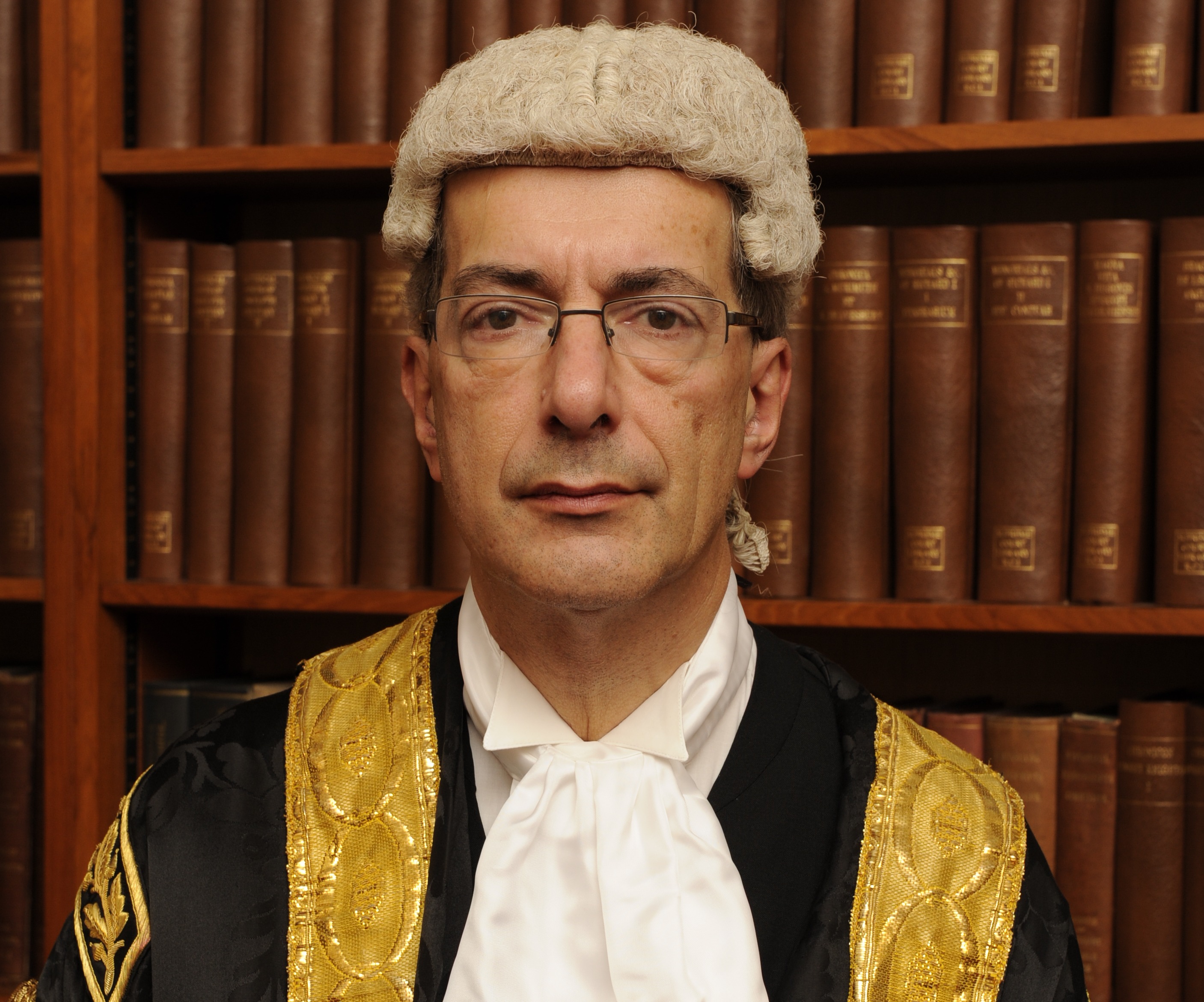 Justice Bean in his judicial robes, wig, and cravat, in front of a bookshelf.