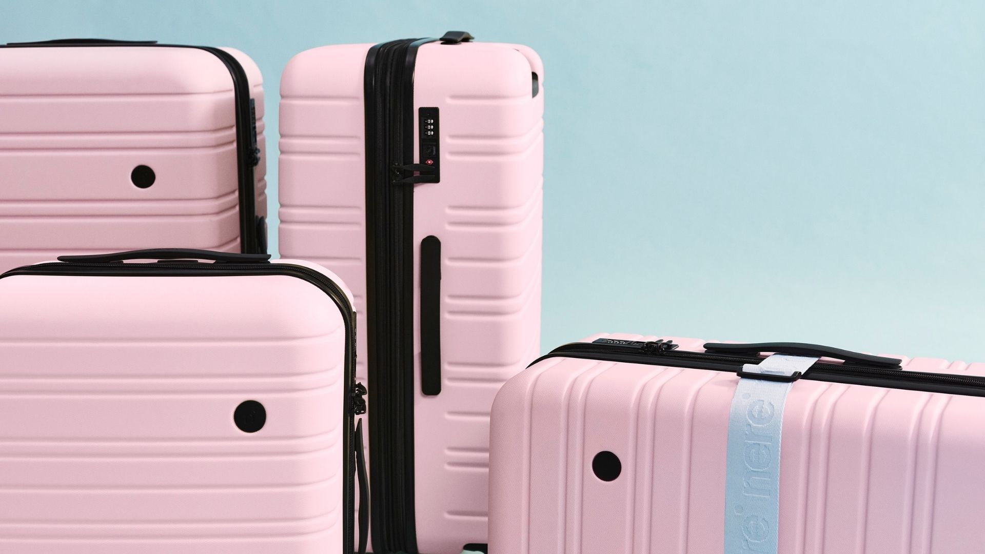 Four pink hard-shell suitcases with black accents, one with a light blue strap, against a light blue background.