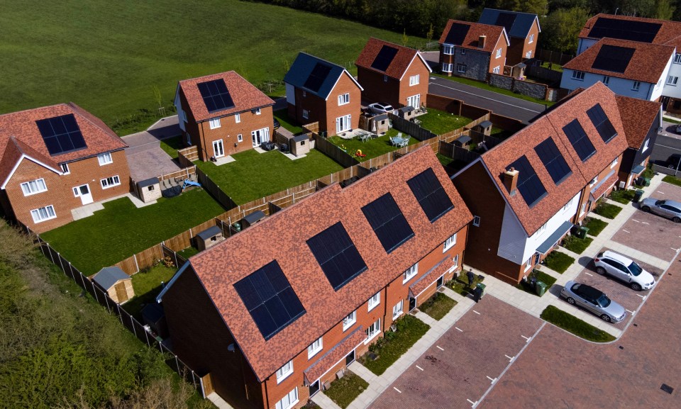 Aerial view of multiple red-roofed houses with solar panels on their roofs, and green lawns.