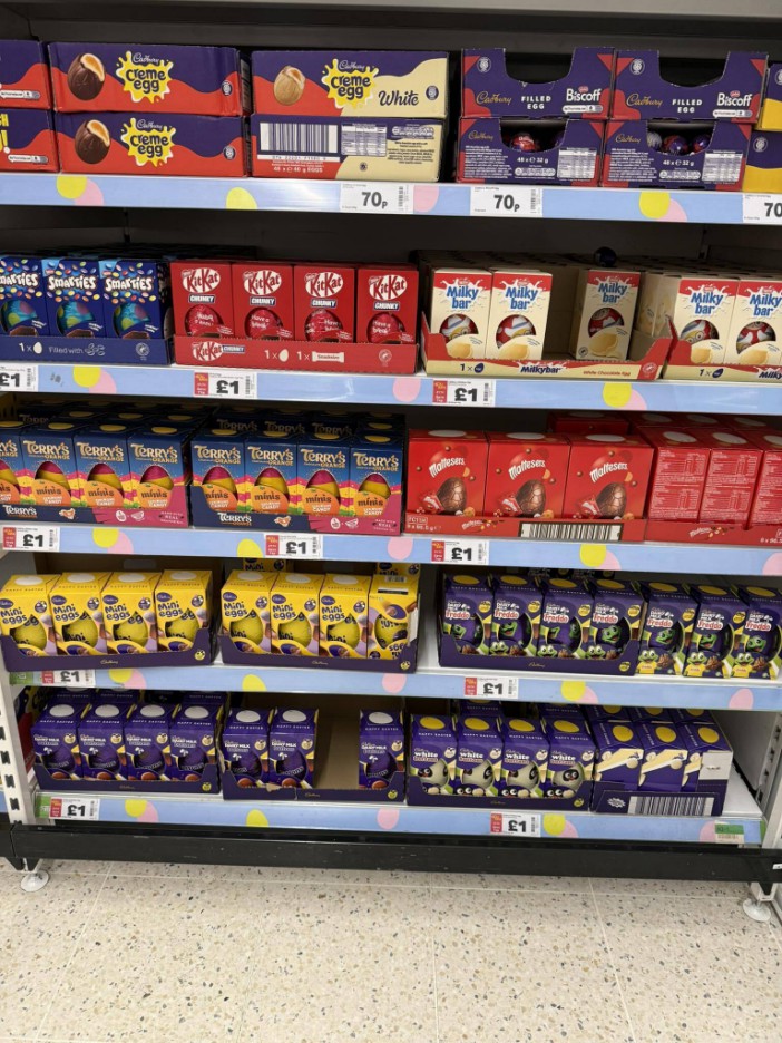 A grocery store shelf filled with various brands of Easter egg candies, including Cadbury Creme Egg, Kit Kat, Milkybar, and Mini Eggs.