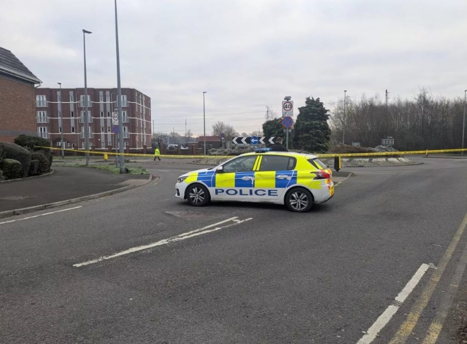 Police car at a cordoned-off scene on a road.