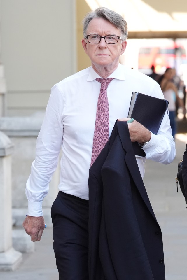 Lord Peter Mandelson, in a white shirt and red tie, holds a dark blue jacket and book while walking.