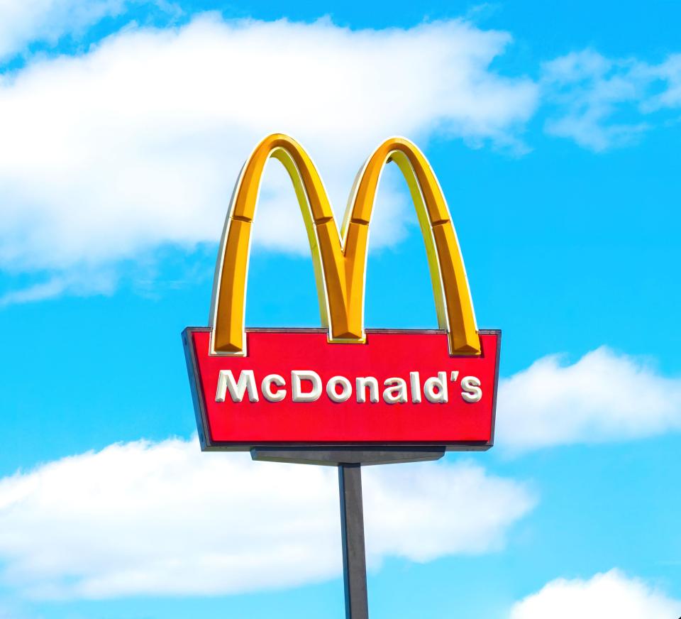 McDonald's golden arches logo and red sign against a blue sky with white clouds.
