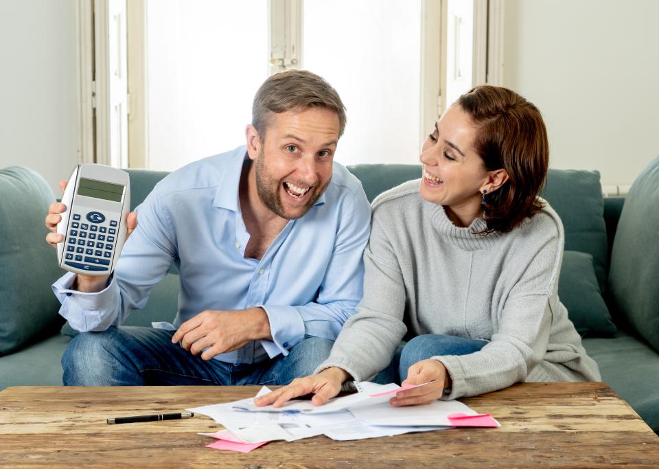 A man holding a calculator and a woman looking at financial documents appear happy and relieved.