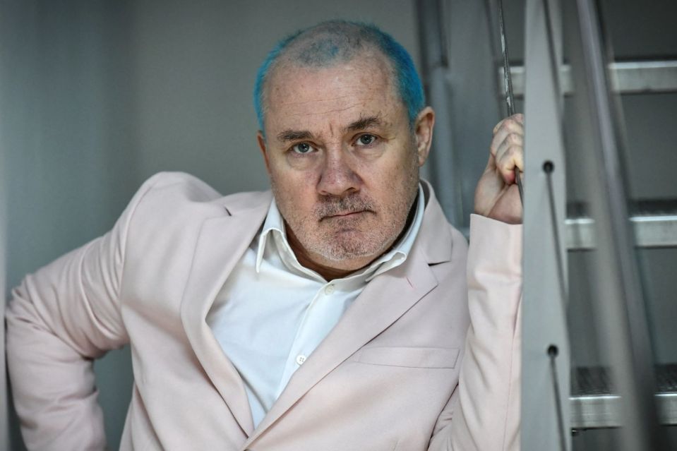 An image collage containing 1 images, Image 1 shows Damien Hirst, a British artist with blue hair, poses in a light pink jacket