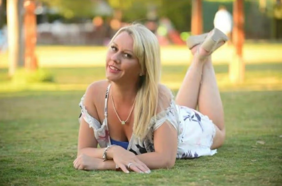 A woman with long blonde hair lies on grass, smiling.