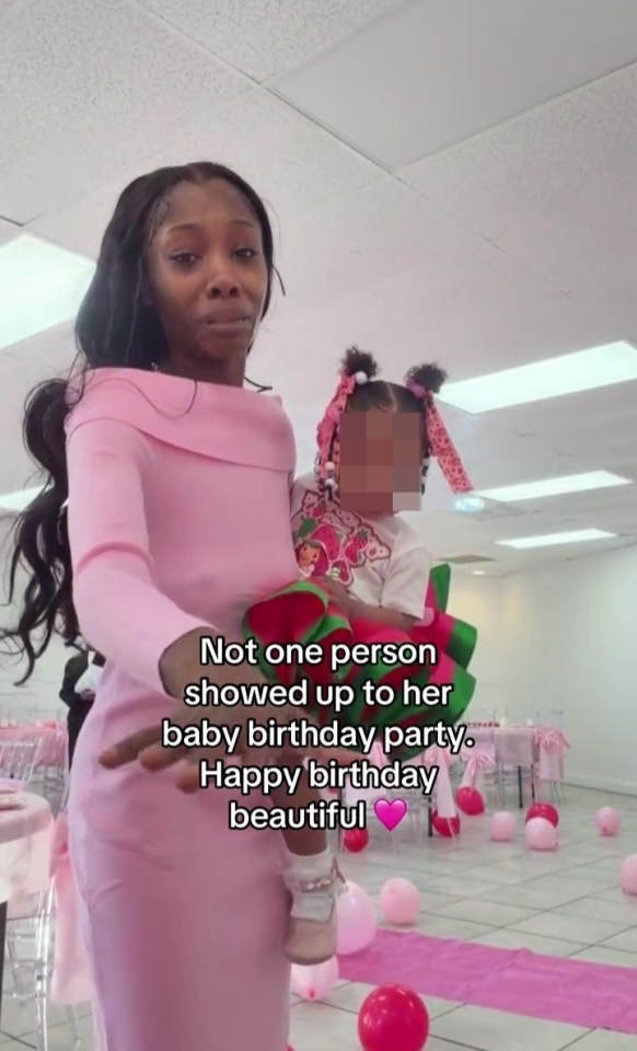 A mother cries while holding her young daughter in an empty party room, decorated with pink balloons and tables.
