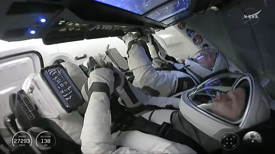 Two astronauts in spacesuits lie inside a spacecraft with digital readouts showing speed and altitude.