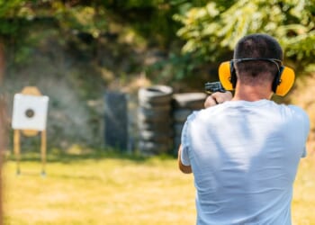 Adult man shooting a target with a handgun in an outdoor shooting range.