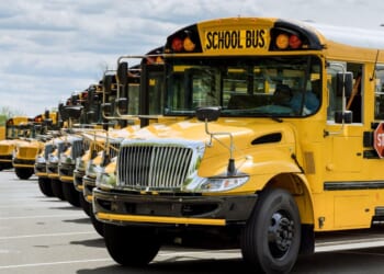 A fleet of yellow school buses parked near a high school.