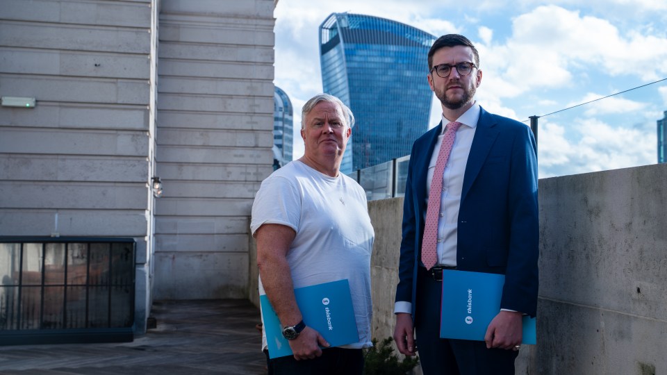 Two men holding blue "thisbank" folders stand outside with a modern building in the background.